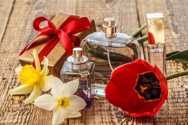 Confezione regalo avvolta con nastro rosso e bottiglie di profumo su tavole di legno con bouquet di tulipano rosso