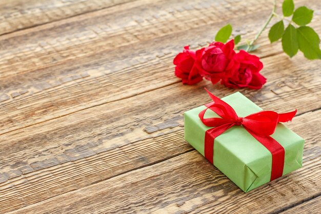 Confezione regalo avvolta con nastro su vecchie tavole di legno decorate con rose rosse Vista dall'alto con spazio per la copia
