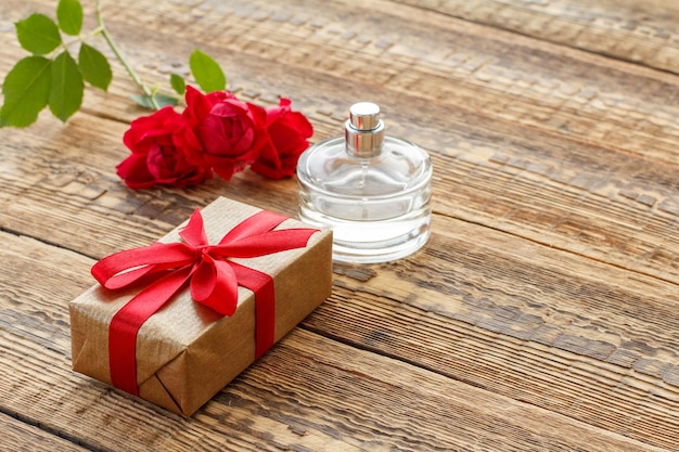 Confezione regalo avvolta con un nastro e una bottiglia di profumo su tavole di legno decorate con rose rosse