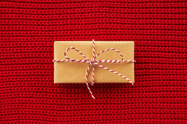 Confezione regalo avvolta in carta artigianale su sfondo rosso a maglia. Vista dall'alto, distesi, copia spazio.