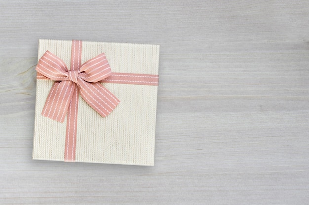 Confezione regalo beige con nastro rosa su fondo di legno con spazio per la copia, regalo per Natale o grazie