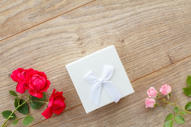 Confezione regalo bianca con bellissime rose su tavole di legno. Concetto di fare un regalo nei giorni festivi. Vista dall'alto.