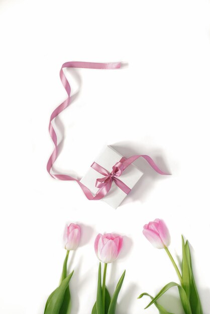 Confezione regalo bianca con fiocco in raso rosa e bouquet di tulipani rosa su sfondo bianco. Biglietto di auguri per la festa della mamma, compleanno, 8 marzo, Pasqua