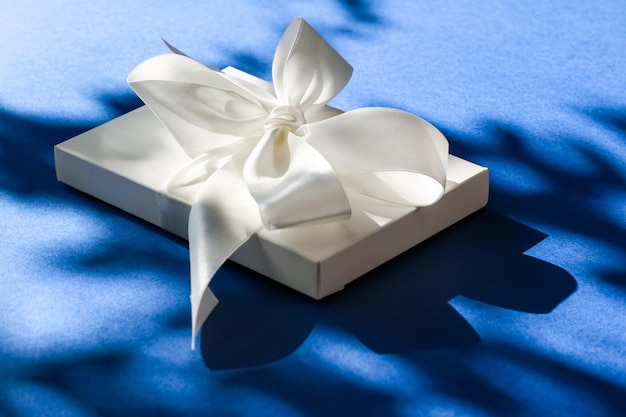 Confezione regalo bianca per vacanze di lusso con nastro di seta e fiocco su sfondo blu regalo di nozze o compleanno di lusso