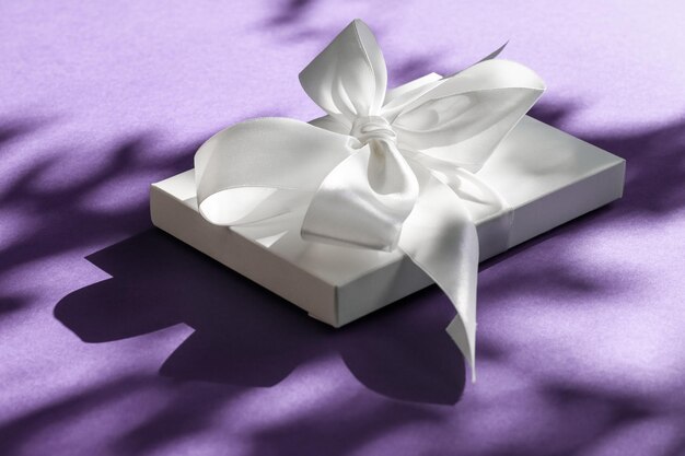Confezione regalo bianca per vacanze di lusso con nastro di seta e fiocco su sfondo viola, matrimonio di lusso o regalo di compleanno