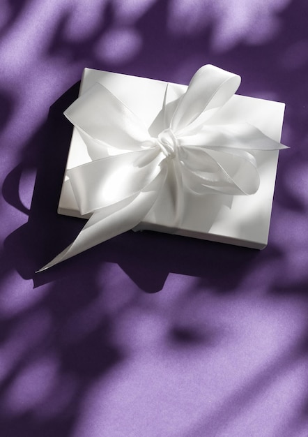 Confezione regalo bianca per vacanze di lusso con nastro di seta e fiocco su sfondo viola, matrimonio di lusso o regalo di compleanno