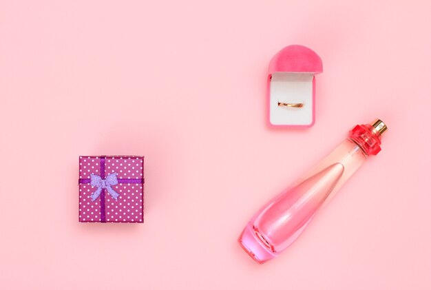 Confezione regalo, bottiglia di profumo e anello dorato in scatola su sfondo rosa. Cosmetici e accessori donna. Vista dall'alto.