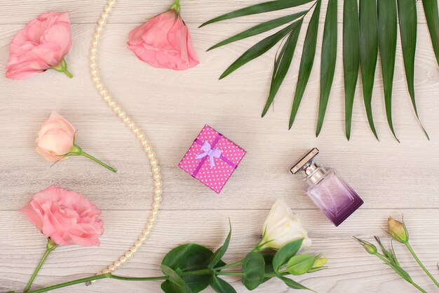 Confezione regalo, bottiglia di profumo, perline su un filo, fiori bianchi e rosa, foglie verdi su fondo di legno. Cosmetici da donna. Vista dall'alto.