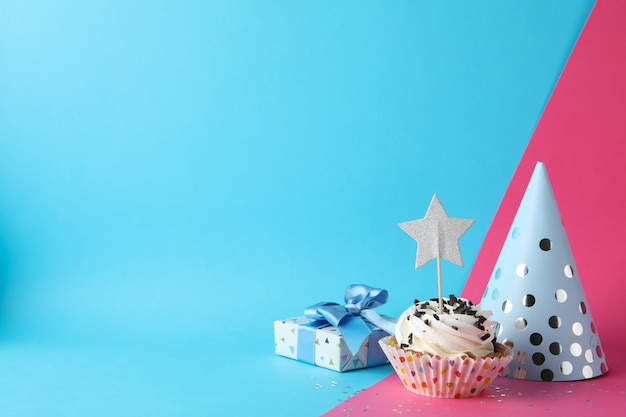 Confezione regalo, cappello compleanno e cupcake su uno sfondo di due toni, spazio per il testo