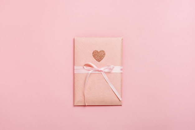 Confezione regalo con cuore su sfondo rosa pastello.