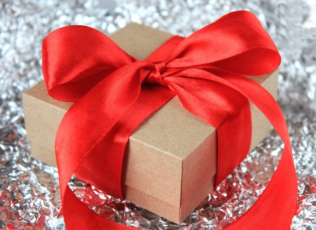 Confezione regalo con fiocco in nastro rosso su superficie scintillante