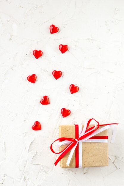 Confezione regalo con fiocco rosso e bianco e cuori sul tavolo bianco per San Valentino. Vista dall'alto con copia spazio