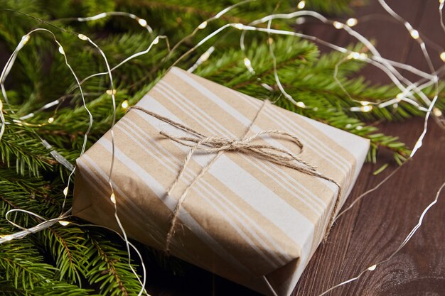 Confezione regalo con luce di Natale e rami di abete verde su fondo di legno marrone