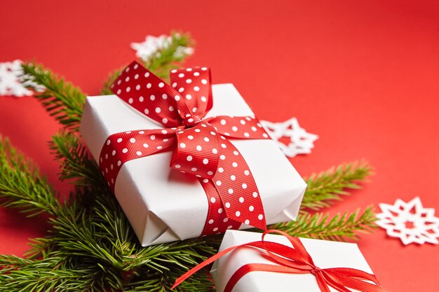 Confezione regalo con ramo di albero di Natale e fiocchi di neve bianchi su sfondo rosso