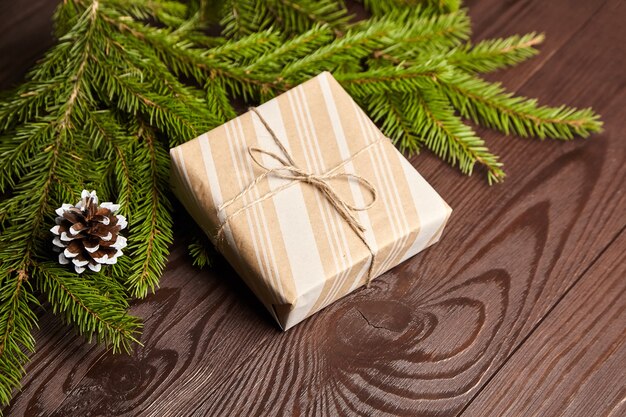 Confezione regalo con ramo di albero di Natale verde e cono su fondo di legno marrone