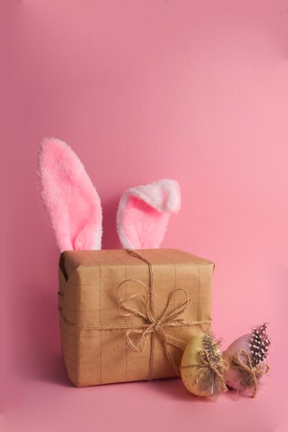 Confezione regalo con simpatiche orecchie da coniglio e uova di pasqua su sfondo rosa spazio copia