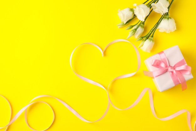 Confezione regalo, cuore in nastro e rose su sfondo giallo