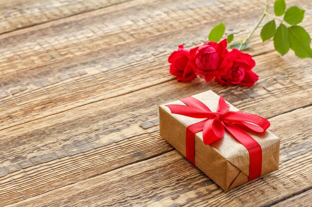Confezione regalo decorata con nastro e bouquet di rose rosse su vecchie tavole di legno Vista dall'alto