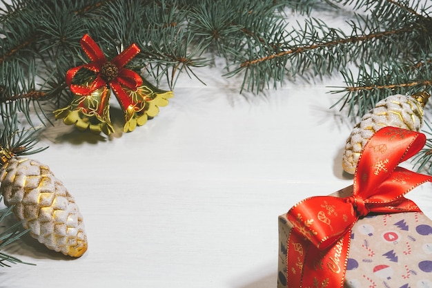 Confezione regalo decorata su sfondo bianco con campane di Natale e rami di pino e coni