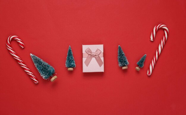 Confezione regalo di bastoncini di zucchero a strisce di Natale e mini alberi di Natale su sfondo rosso Sfondo di Natale di Capodanno