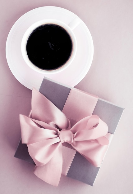 Confezione regalo di lusso e tazza di caffè su sfondo rosa cipria con design flatlay per vacanze romantiche e sorprese di compleanno