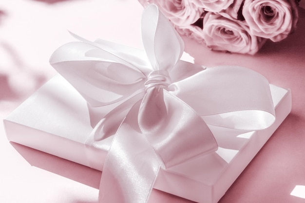 Confezione regalo di lusso in seta per vacanze e bouquet di rose su sfondo rosa cipria sorpresa romantica e fiori come regalo di compleanno o di San Valentino