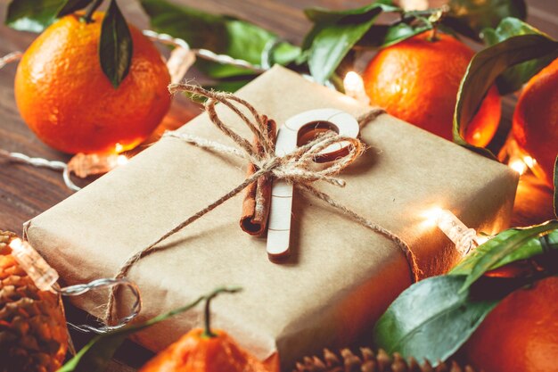 Confezione regalo di Natale in carta kraft tra mandarini e pigne su una tavola festiva Il concetto di accoglienti vacanze invernali