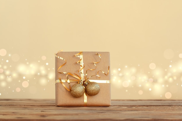 Confezione regalo di Natale o regalo decorato con nastro dorato e due palline su sfondo neutro con boke.