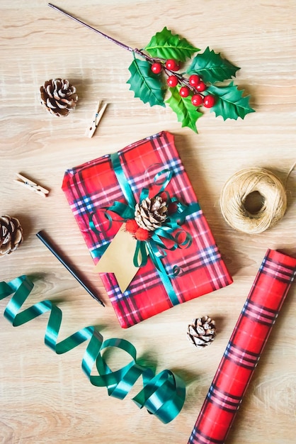 Confezione regalo di Natale piatta in carta fantasia tartan con materiali da imballaggio su sfondo di legno