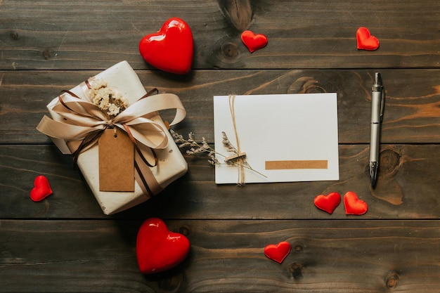 Confezione regalo e biglietto di auguri con fiocco e cuori di carta su tavola di legno per San Valentino. copia spazio.