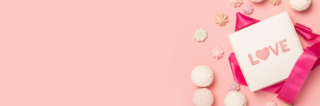 Confezione regalo e caramelle regalo, marshmallow e meringhe su una superficie rosa pastello