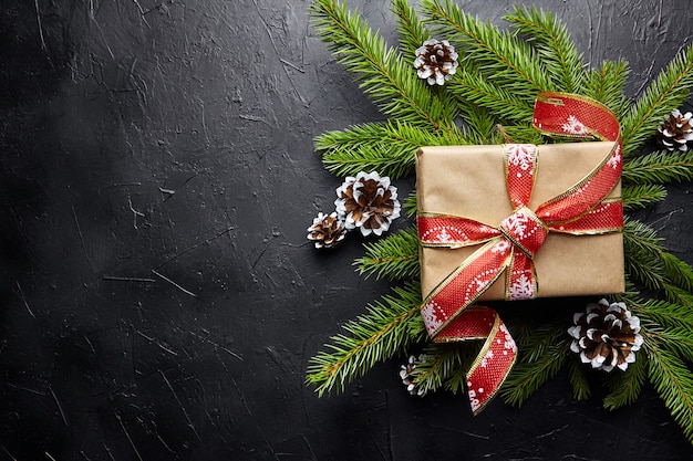 Confezione regalo e ramo di albero di Natale verde con cono su sfondo nero vista dall'alto