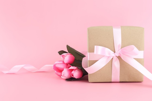 Confezione regalo in carta marrone con fiocco rosa in raso ricci su sfondo rosa pastello Festa della mamma piatta