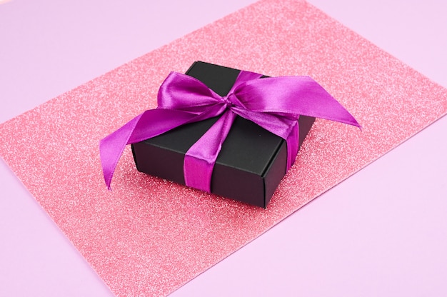 Confezione regalo nera con fiocco viola su sfondo rosa