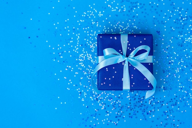 Confezione regalo o regalo legata con un nastro blu su sfondo di carta blu con brillantezza