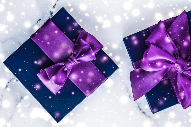 Confezione regalo per le vacanze invernali con fiocco di seta viola con glitter di neve su sfondo marmoreo come regali di Natale e Capodanno per un design flatlay di lusso di marca di bellezza