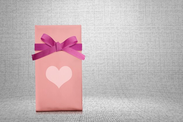 Confezione regalo rosa con nastro rosso e cuore con sfondo a trama