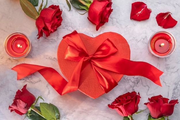 Confezione regalo rossa a forma di cuore con fiocco in raso circondato da rose e candele