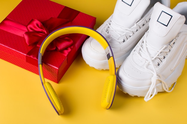 Confezione regalo rossa di scarpe da ginnastica e cuffie con marchio bianco. Su sfondo giallo