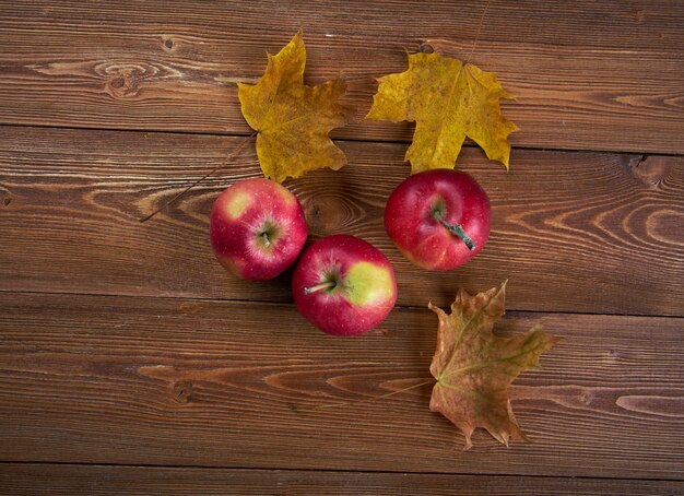 Confine autunnale di mele e foglie cadute sul vecchio tavolo di legno.