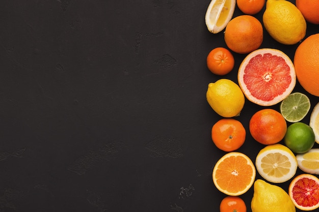 Confine di agrumi assortiti su sfondo nero, copia spazio. Vista dall'alto su arance, limoni, mandarini e bicchieri di succo, distesi. Fare il concetto di detox fresco e il mockup della ricetta