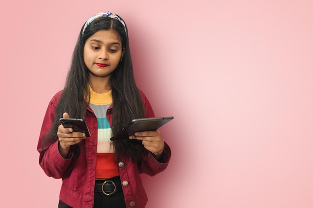 Confuso giovane indiano asiatico adolescente in posa isolato sorridente e messaggistica sul telefono cellulare e tablet utilizzando entrambe le mani con lo spazio della copia mockup