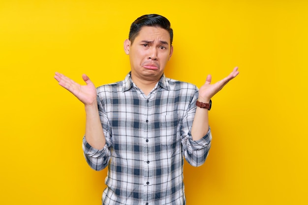 Confuso giovane uomo asiatico bello che indossa una camicia a quadri In piedi allargando la mano reagendo a qualcosa di isolato su sfondo giallo Concetto di stile di vita delle persone