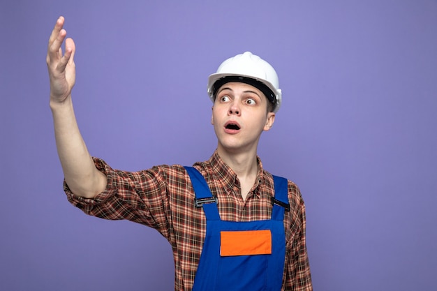 Confuso guardando lato alzando la mano giovane costruttore maschio che indossa l'uniforme