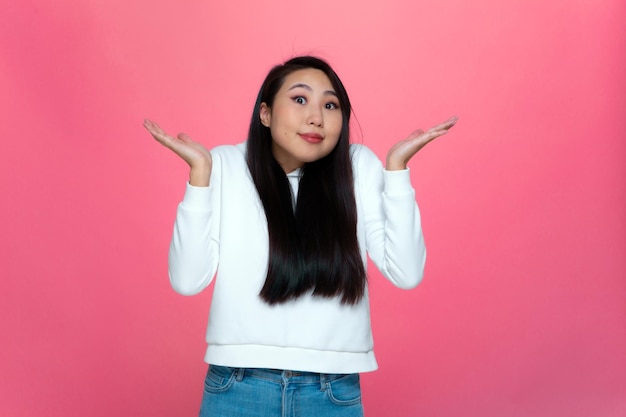 Confuso positivo perplesso giovane ragazza asiatica scrollò le spalle alzando i palmi delle mani non so rispondere su sfondo rosa studio Foto di alta qualità