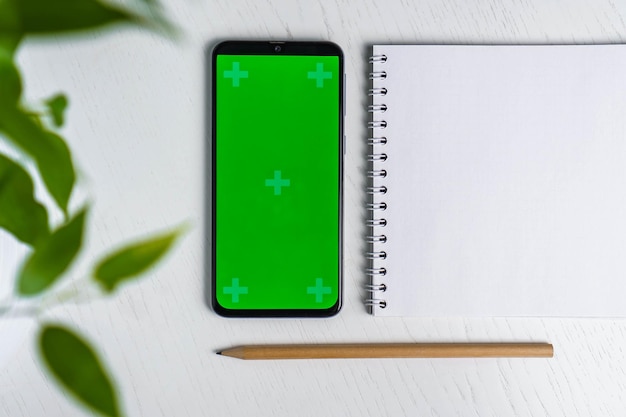 Congedo verde con mockup di schermo verde per smartphone con blocco note vuoto e disposizione piatta della matita Vista dall'alto