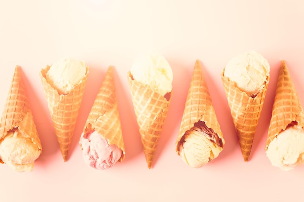Coni gelato di cialda con piatto di palline di gelato su sfondo rosa.