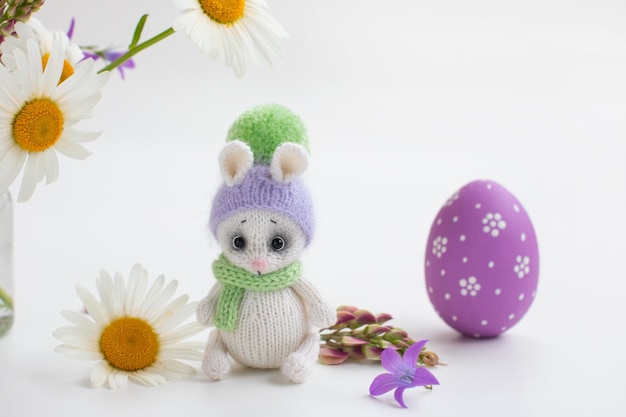 Coniglietto di Pasqua lavorato a maglia con uova dipinte su sfondo bianco Mazzo primaverile di margherite con composizione pasquale