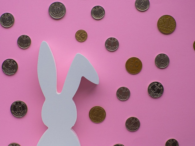 Coniglietto pasquale bianco circondato da monete su sfondo rosa