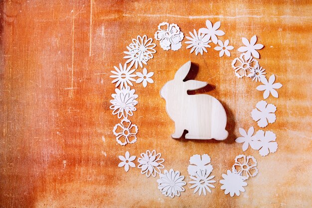 Coniglio di coniglietto di pasqua con diversi fiori di carta intorno sopra il muro di pietra arancione. Lay piatto, copia dello spazio. vacanze di Pasqua